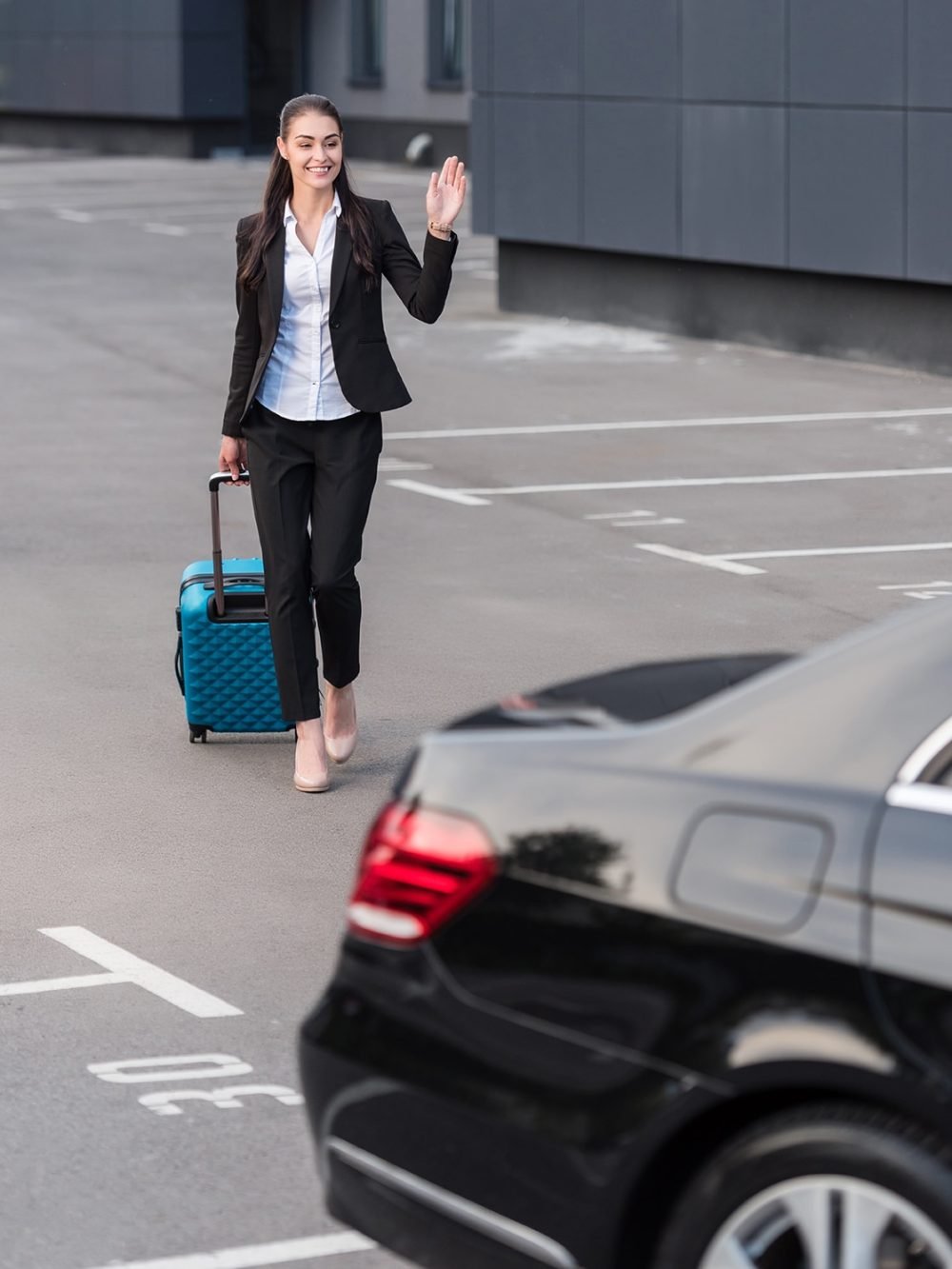 Young woman in pant suit walking towards passenger car with suitcase